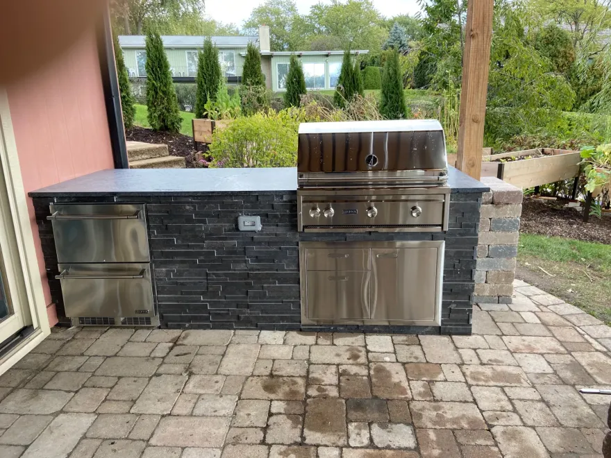Stone outdoor kitchen island with stone-clad prefab base and custom countertop