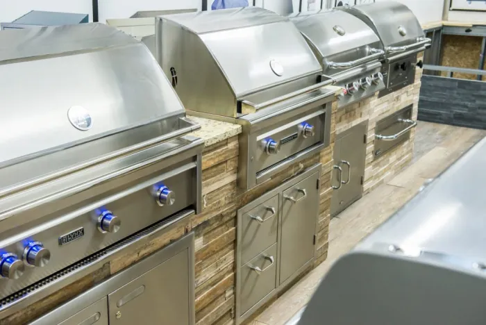 A row of Lynx built-in grills with blue-lit control knobs on stacked-stone islands